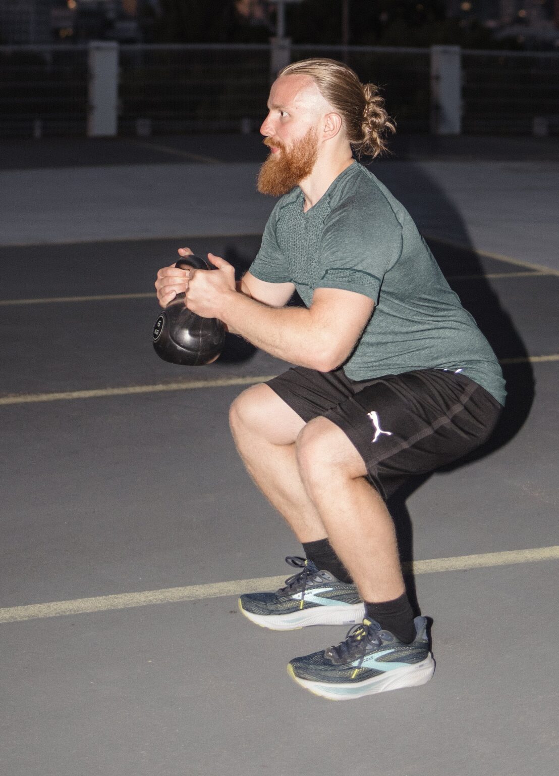 Personal Trainer Matthäus in der tiefen Kniebeuge mit Kettlebell auf einem Parkdeck in Frankfurt am Main