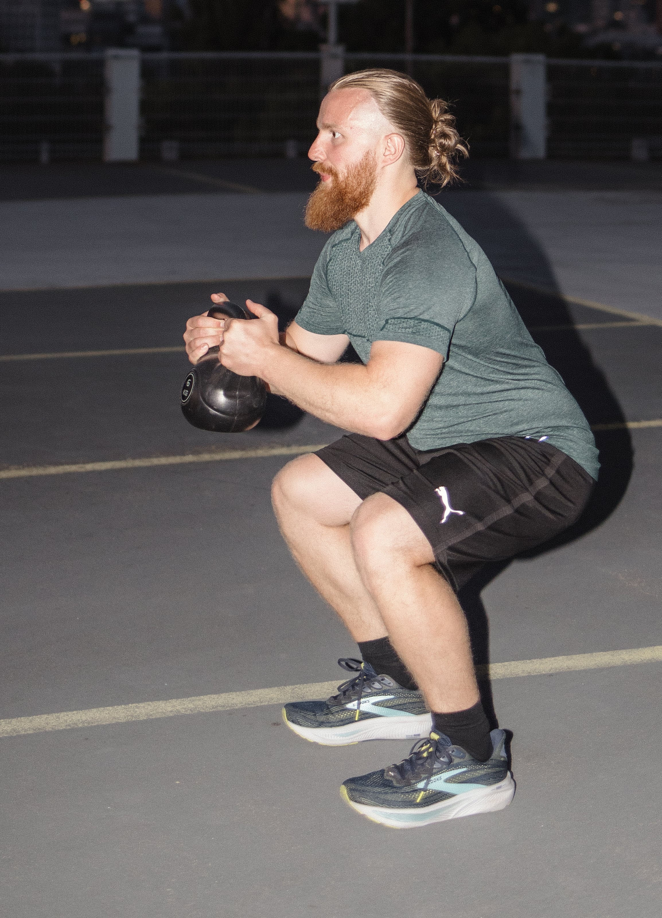 Personal Trainer Matthäus in der tiefen Kniebeuge mit Kettlebell auf einem Parkdeck in Frankfurt am Main