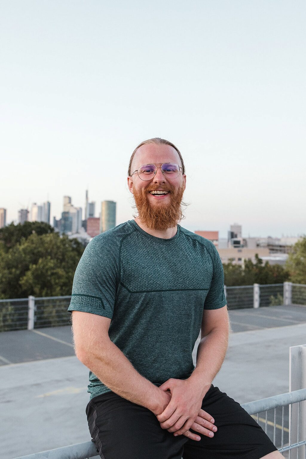 Personal Trainer Matthäus sitzt entspannt auf einem Geländer vor der Frankfurter Skyline