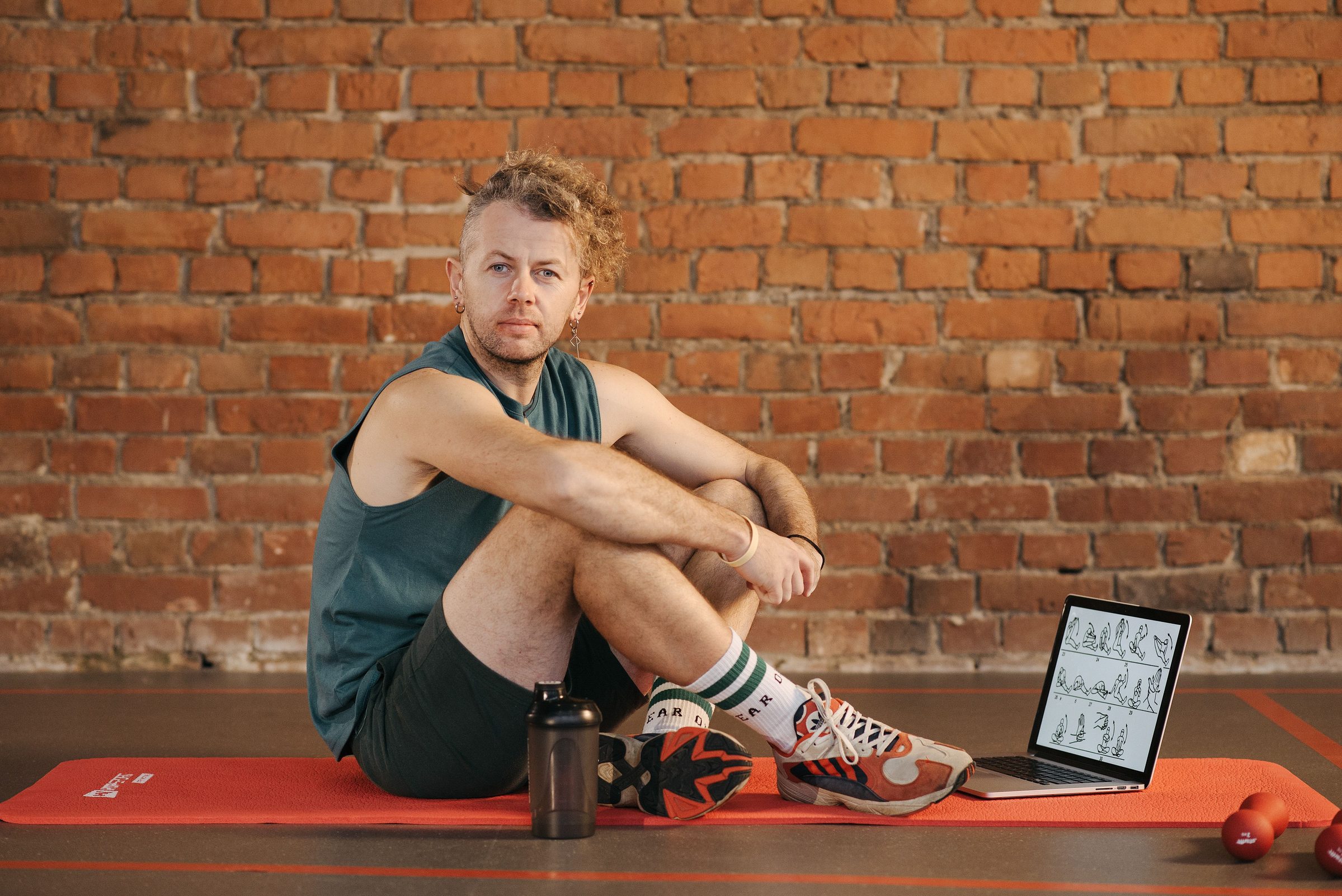 Mann sitzt auf einer Trainingsmatte, daneben ein Laptop mit dem Trainingsplan — Sinnbild für Online-Coaching
