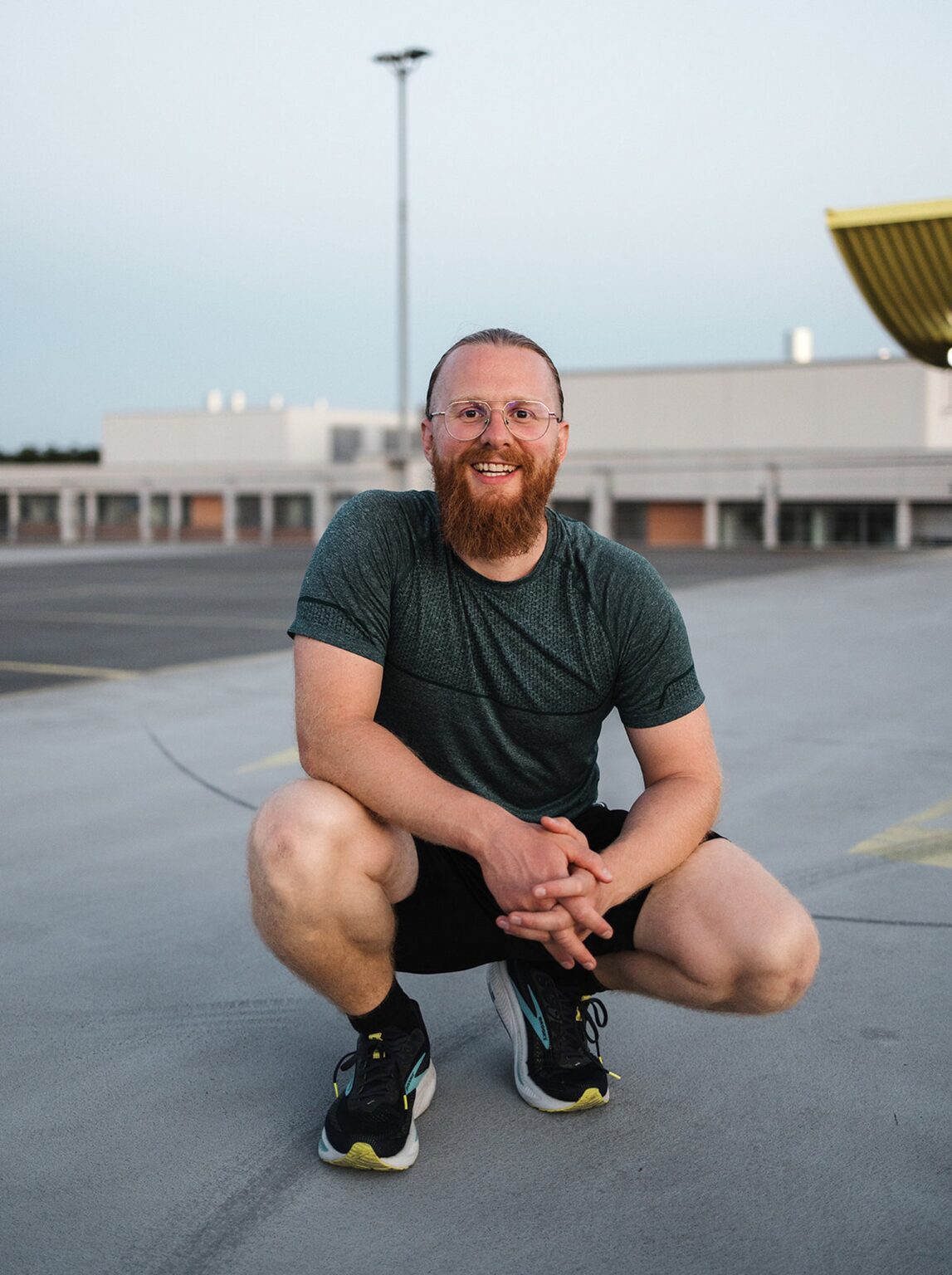 Personal Trainer Matthäus hockt lächelnd auf dem Parkdeck