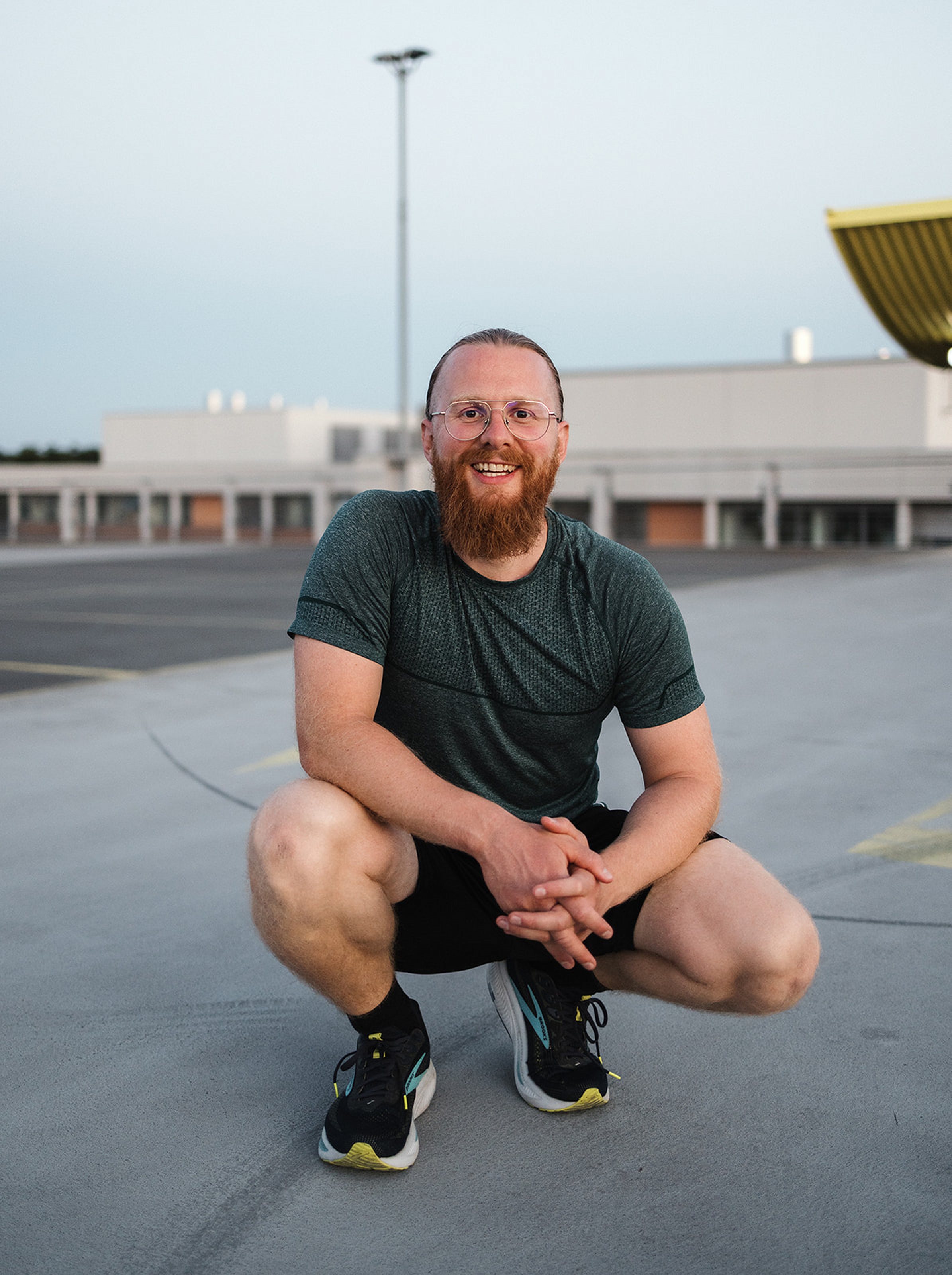Personal Trainer Matthäus hockt lächelnd auf dem Parkdeck