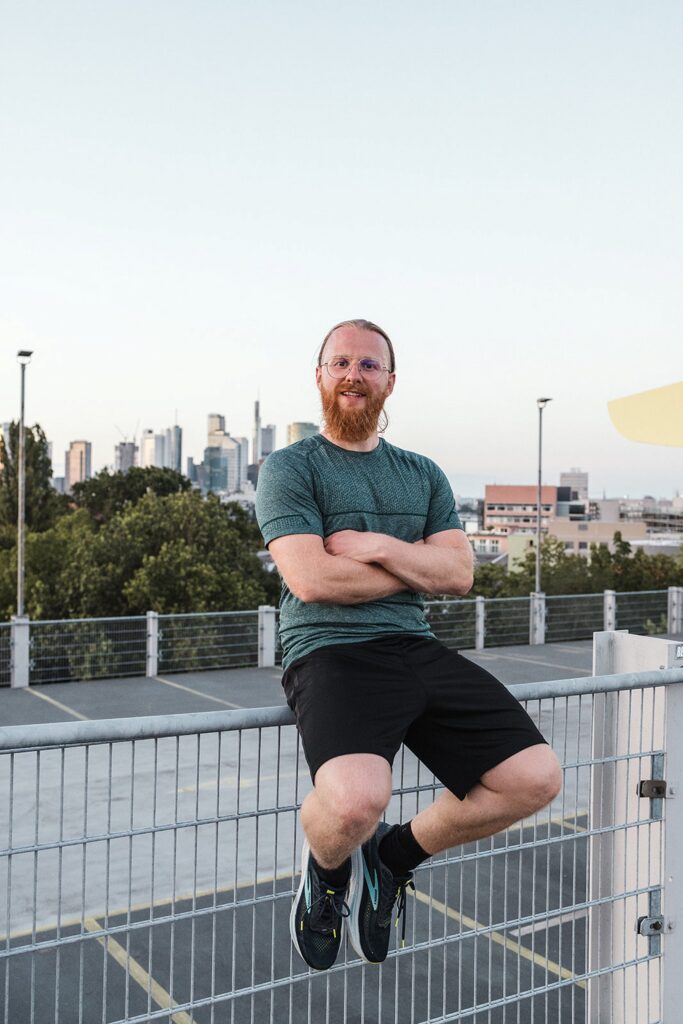 Personal Trainer Matthäus lehnt am Geländer eines Parkdecks in Frankfurt