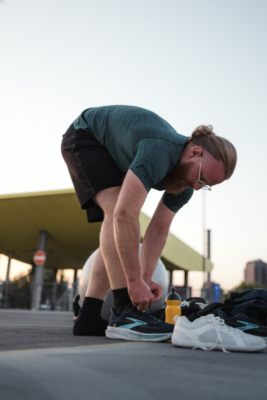 Personal Trainer Matthäus bindet vor dem Training auf einem Frankfurter Parkdeck seine Laufschuhe, daneben Gymnastikball, Trinkflasche und Tasche